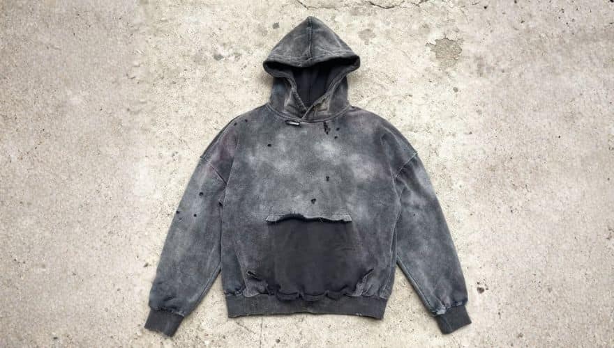 Black destroy wash hoodies laid flat on green artificial grass, featuring a faded charcoal finish, gothic style giving a distressed vintage streetwear look.