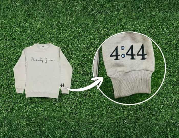 Personalized embroidered sweatshirt with 4:44 cuff detail client example, cream pullover custom printing and embroidery service showcase on grass background.